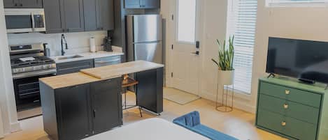 A compact kitchen with modern appliances, a dining area with a table and chairs, and a green cabinet with a television.