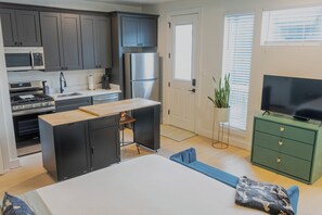 Une cuisine compacte dotée d’appareils électroménagers modernes, un coin repas avec une table et des chaises, et un meuble vert abritant un téléviseur.