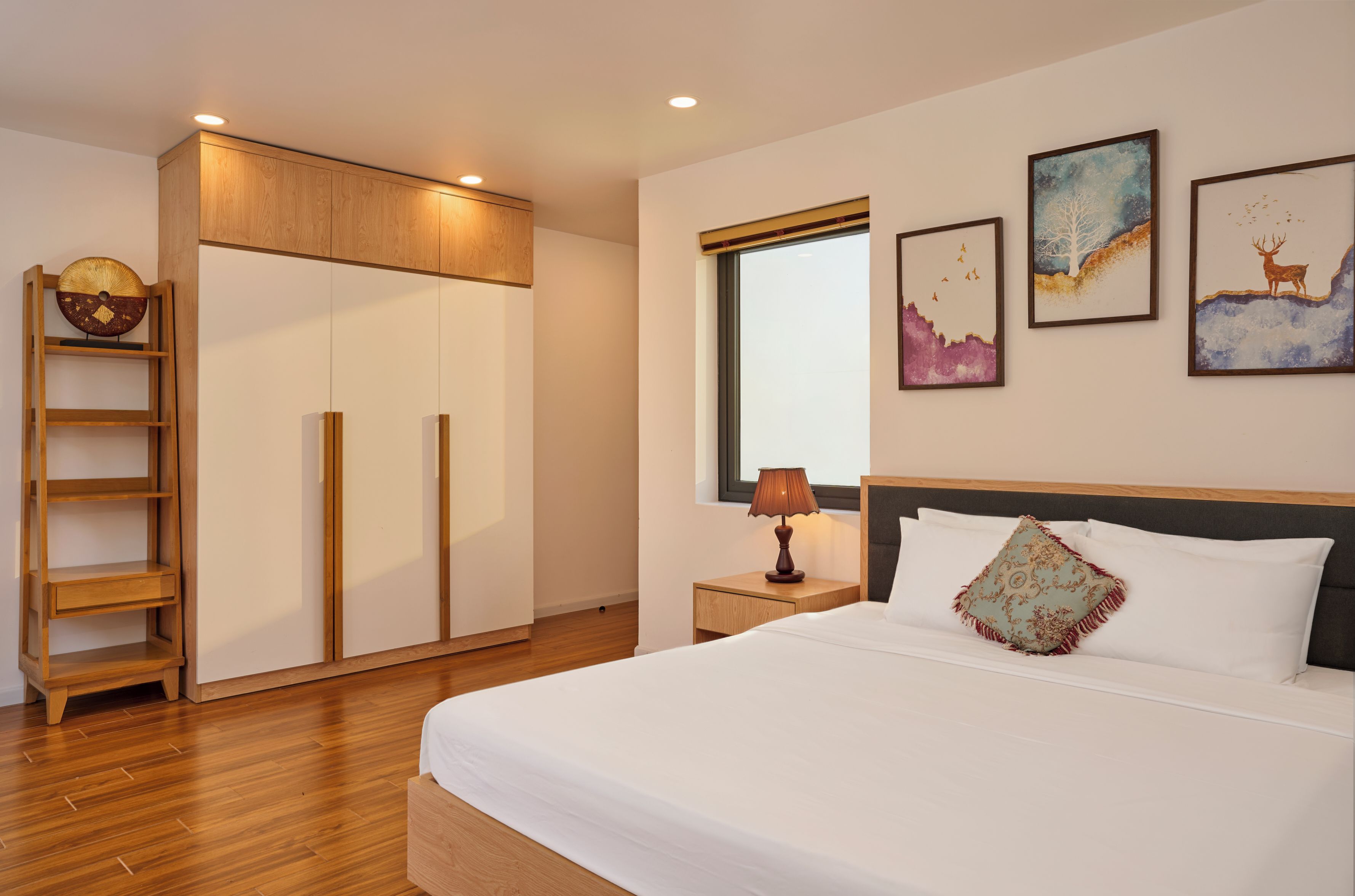 A hotel room with a bed, a nightstand, a lamp, a wardrobe, and artwork on the wall.