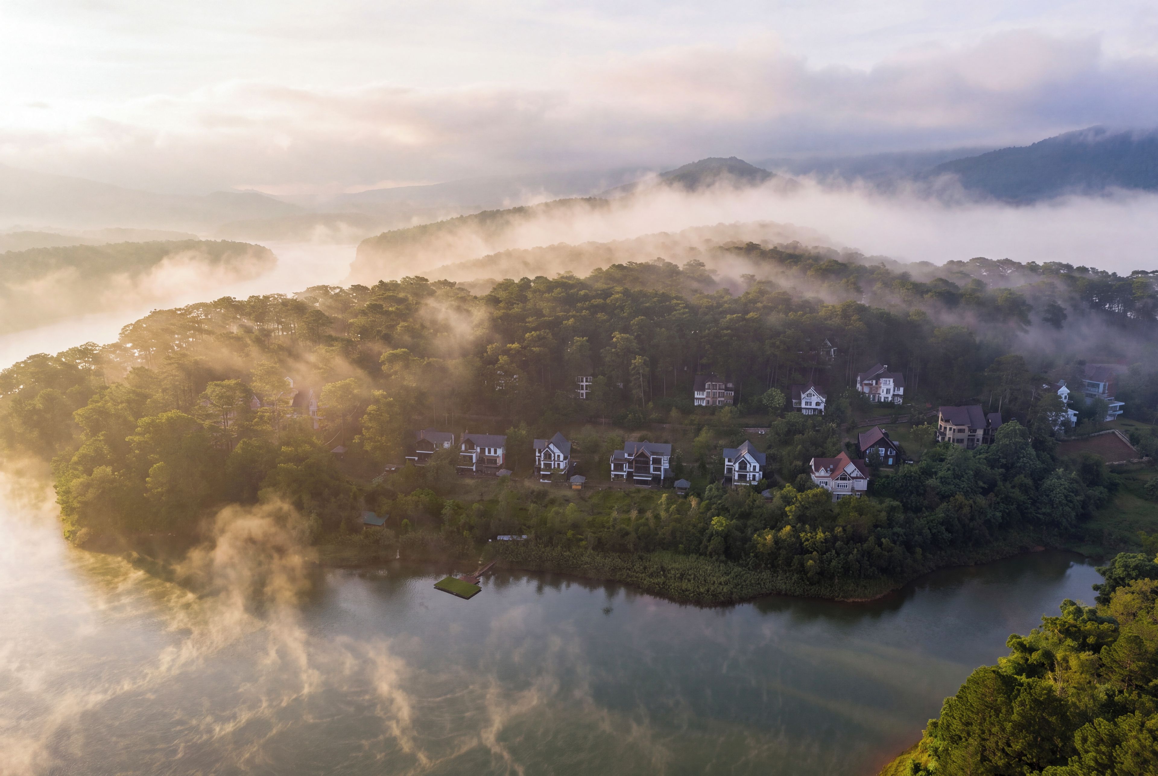 A lakeside village with houses surrounded by forested hills and mist.
