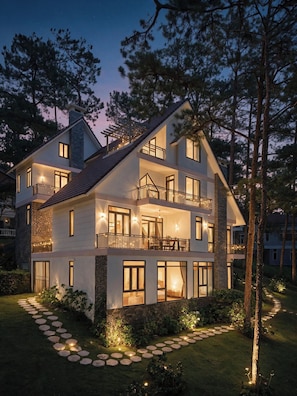 A multi-story house with a stone facade, multiple balconies, and a well-lit garden path.