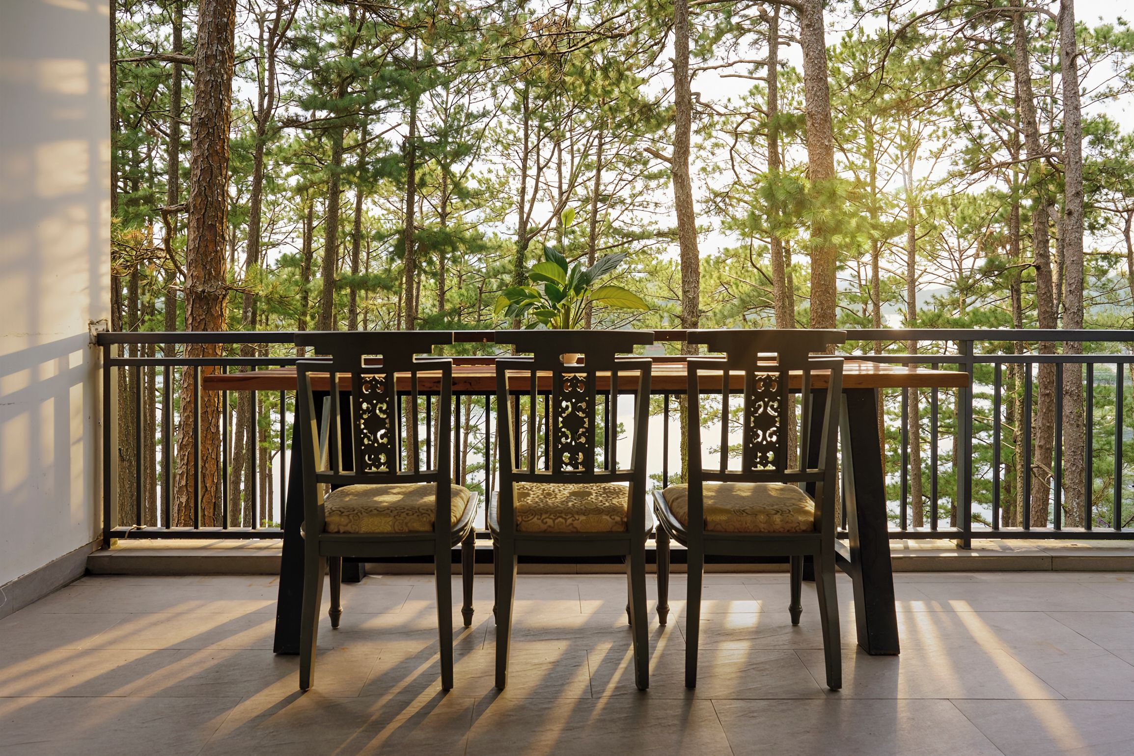 A balcony with a wooden table and chairs, overlooking a forested area.