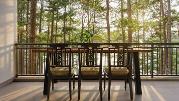 A balcony with a wooden table and chairs, overlooking a forested area.