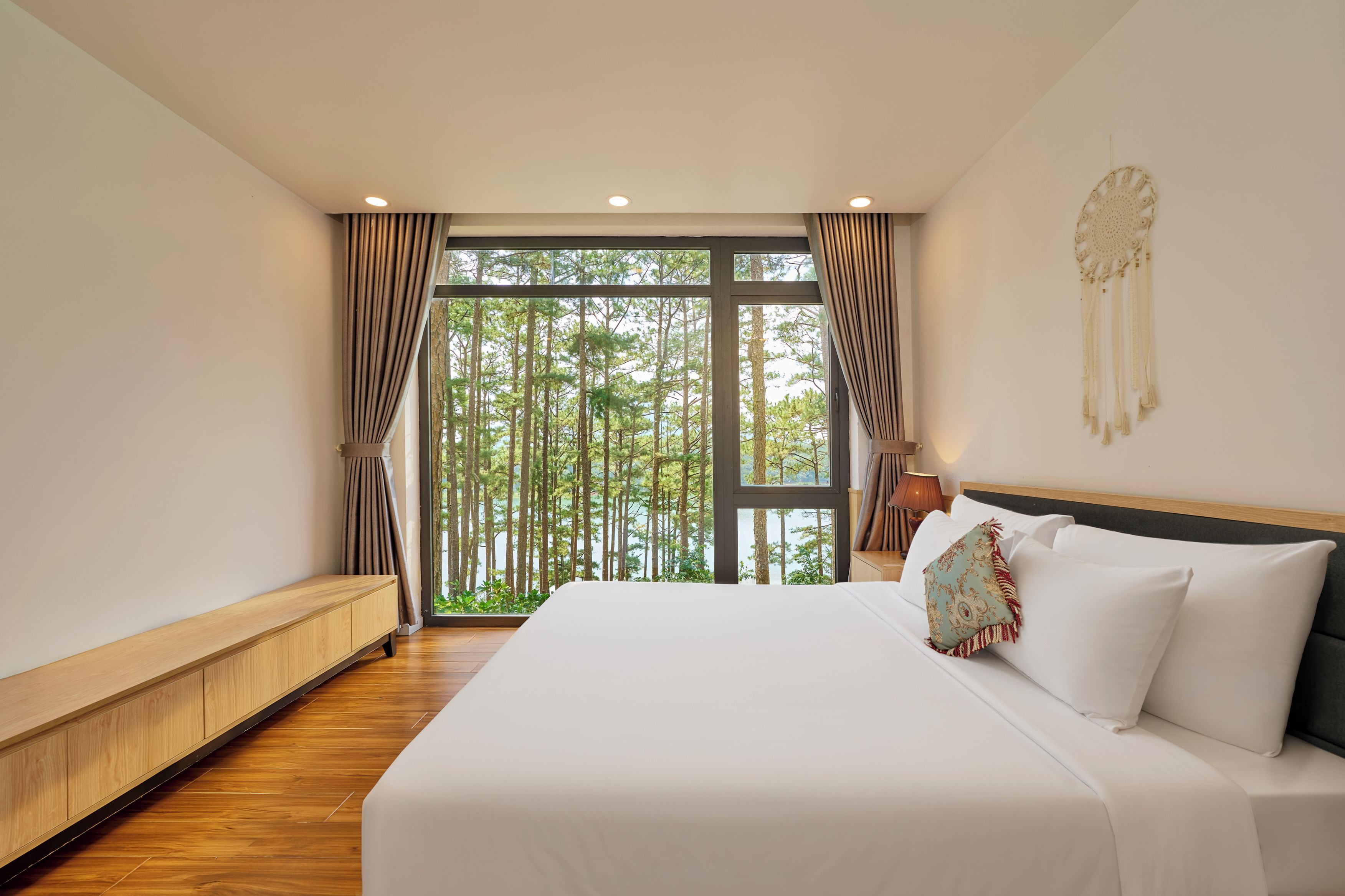 Ein Schlafzimmer mit einem großen Bett, Holzboden und Blick auf Bäume durch ein Fenster.