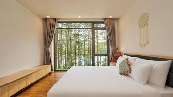Ein Schlafzimmer mit einem großen Bett, Holzboden und Blick auf Bäume durch ein Fenster.