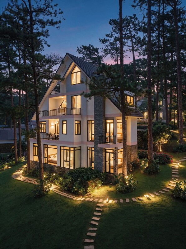 A multi-story house with a balcony, surrounded by trees and a well-lit garden path.