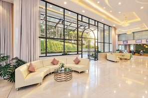 A spacious lobby with a large seating area, a glass coffee table, and a view of a landscaped garden through large windows.