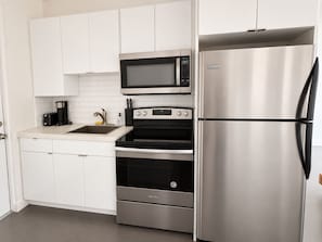 A modern kitchen with white cabinets, a stainless steel refrigerator, a microwave, and an oven. - Modern Studio with Pool near Miami Beach (Miami)