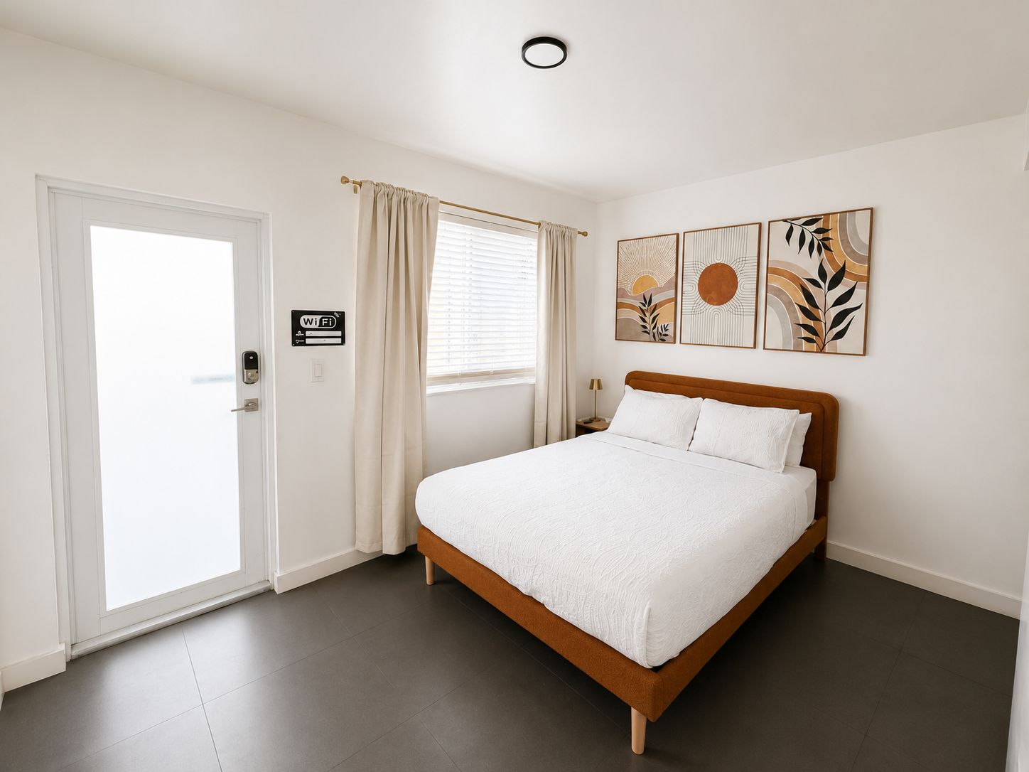 Une chambre à coucher avec un lit, une porte, une fenêtre avec des rideaux et des œuvres d’art murales.