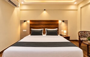 A hotel room with a large bed, a wooden headboard, bedside lamps, a telephone, and a floral armchair. - East Land Hotel Near Manyata Tech (Bengaluru)