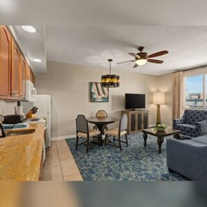 A hotel room with a kitchenette, a dining area with a table and chairs, a sofa, a TV, and a ceiling fan. - Club Wyndham Grand Desert (Las Vegas)