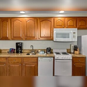 A kitchen with wooden cabinets, a microwave, a stove, and a dishwasher. - Club Wyndham Grand Desert (Las Vegas)