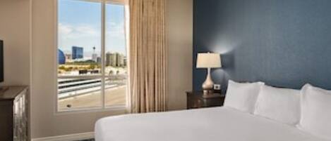 A hotel room with a large bed, a nightstand, a lamp, a ceiling fan, and a window with a view of the city.