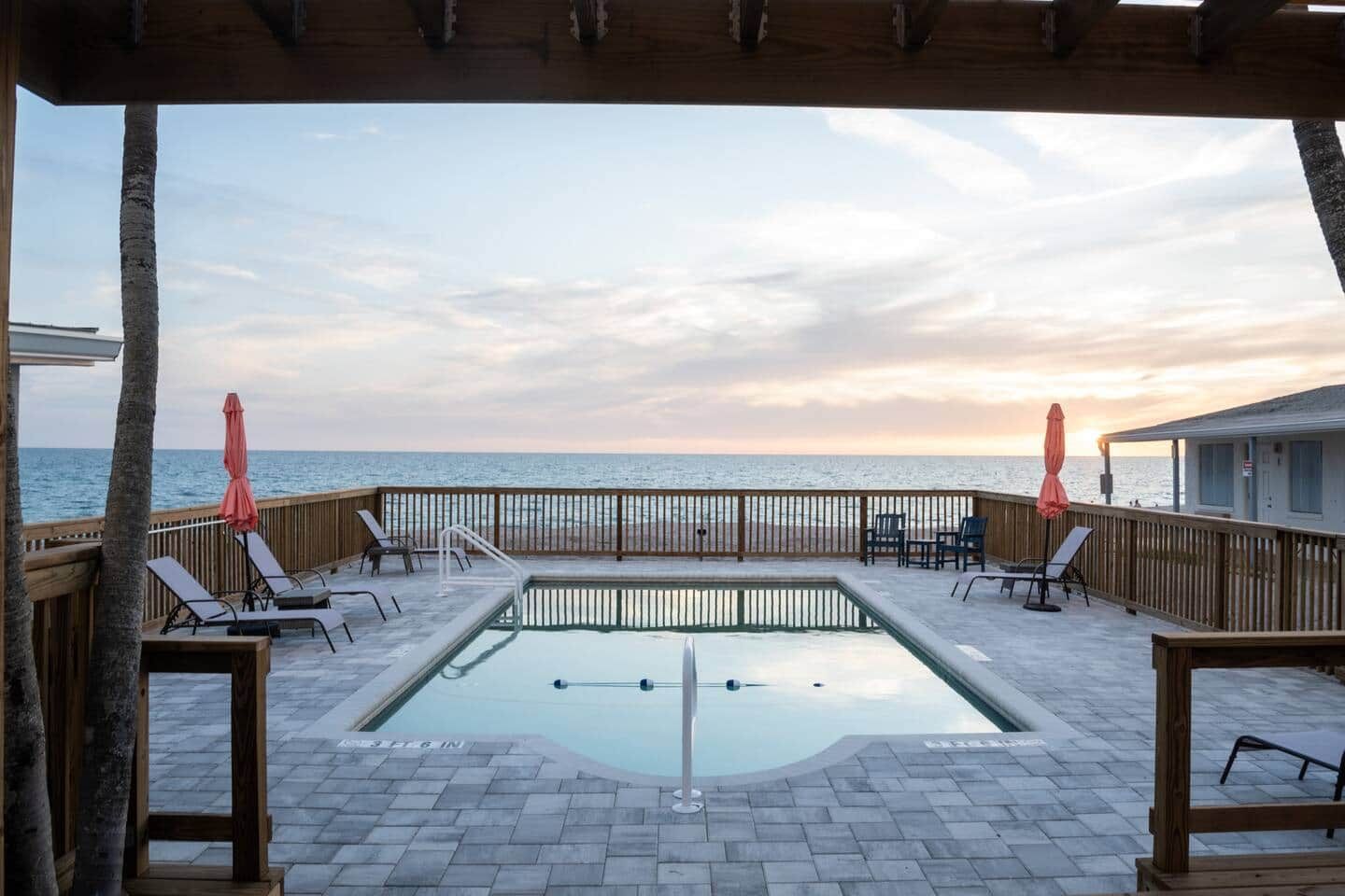 Un espace piscine avec vue sur l’océan, une terrasse en bois et des chaises longues.