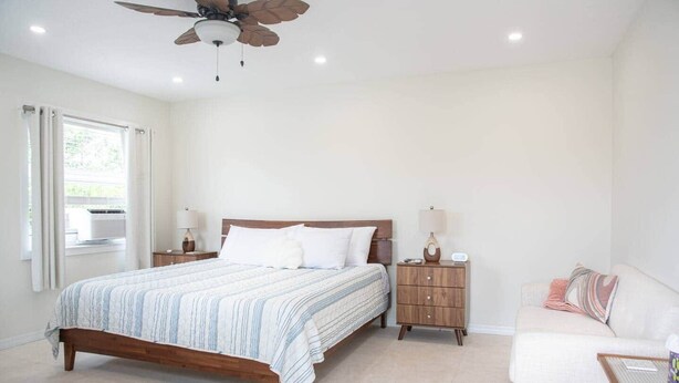 A bedroom with a bed, bedside tables, a ceiling fan, a window with curtains, and a sofa. - #8 Beach Access King Studio (Sarasota County)