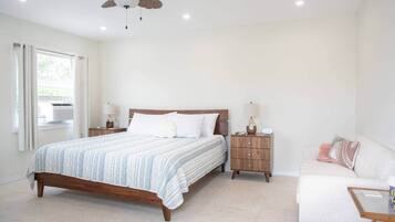 A bedroom with a bed, bedside tables, a ceiling fan, a window with curtains, and a sofa.