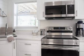 A modern kitchen with stainless steel appliances, a window with blinds, and a coffee maker.