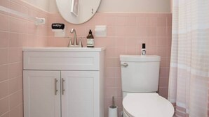 A bathroom with a white sink, mirror, and toilet, pink tiles, and a shower curtain. - #8 Beach Access King Studio (Sarasota County)