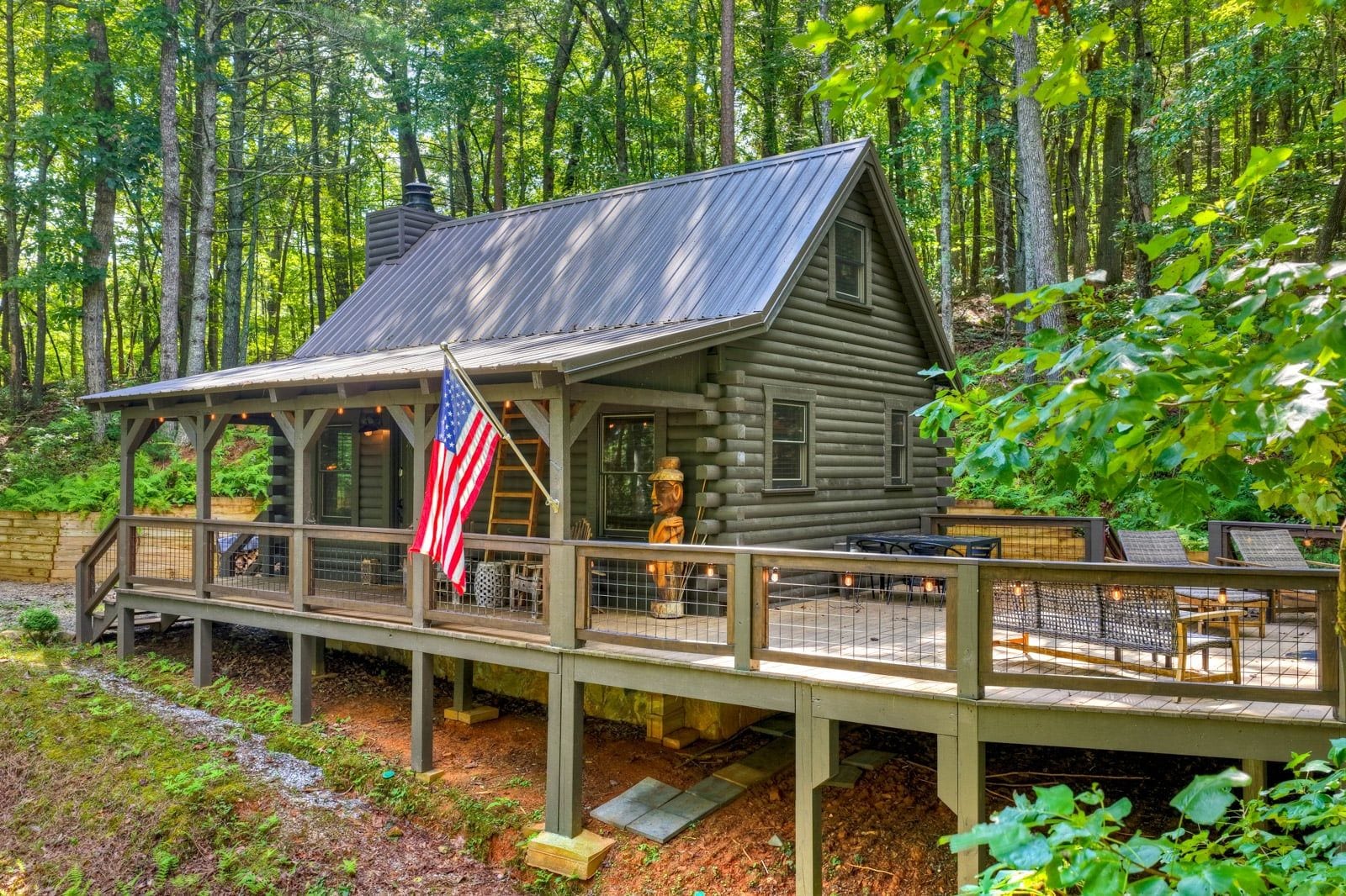 A rustic cabin with a deck, an American flag, and a statue.