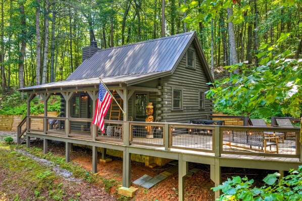 Una baita rustica con una veranda, una bandiera americana e una statua.