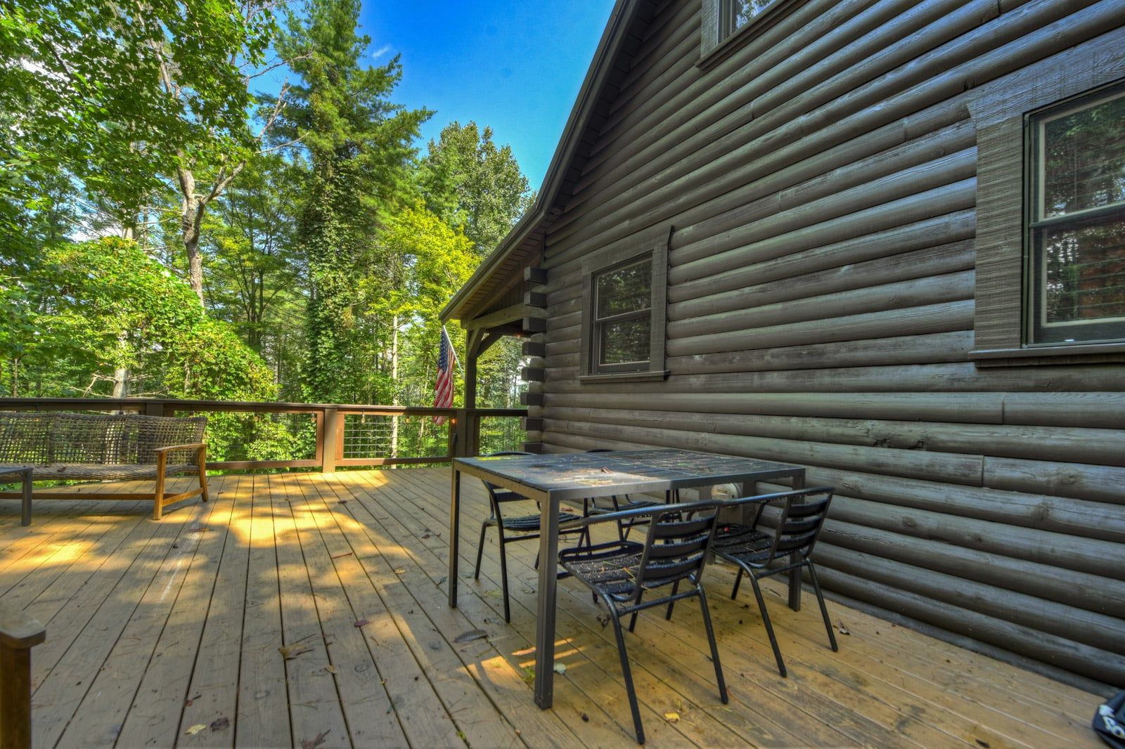 A wooden deck with a table and chairs, surrounded by trees.