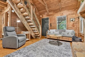 A wooden interior with a staircase, grey sofa, and a small round table. - Piney Mountain Perch - Secluded Log Cabin with Firepit + Fireplace (Mineral Bluff)
