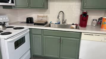A kitchen with green cabinets, a white stove, a sink, and a coffee maker.