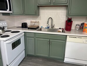 Una cocina con armarios verdes, una estufa blanca, un lavamanos y una cafetera.