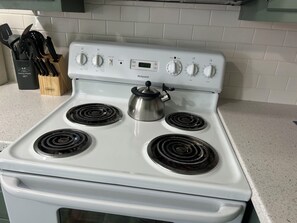 Una estufa blanca con cuatro quemadores, un reloj digital y una olla sobre el quemador delantero.