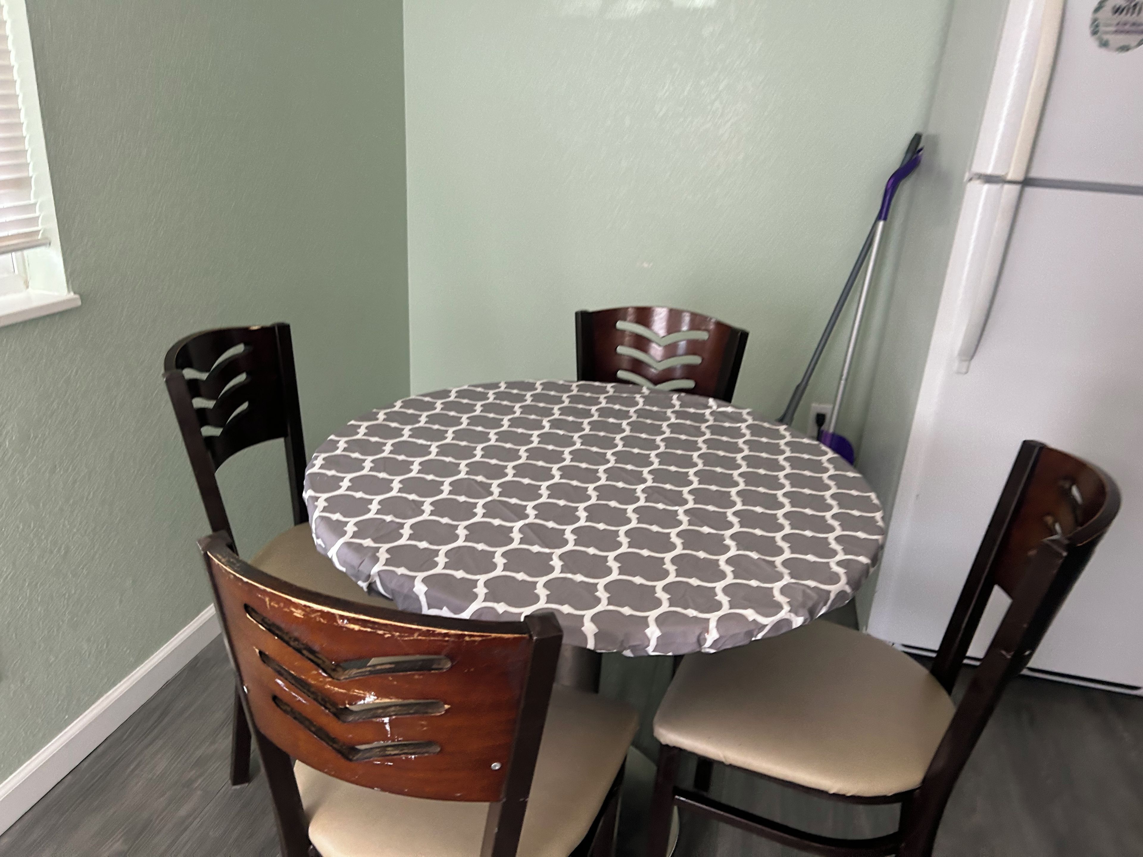 Una mesa de comedor redonda con un mantel estampado, rodeada por cuatro sillas de madera con asientos acolchados.