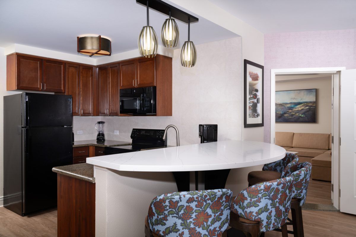 A modern kitchen with wooden cabinets, a black refrigerator, a microwave, and a large island with bar stools.