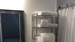 Et badeværelse med toilet, vask, spejl, et håndklædestativ med håndklæder og en bruseforhæng.
