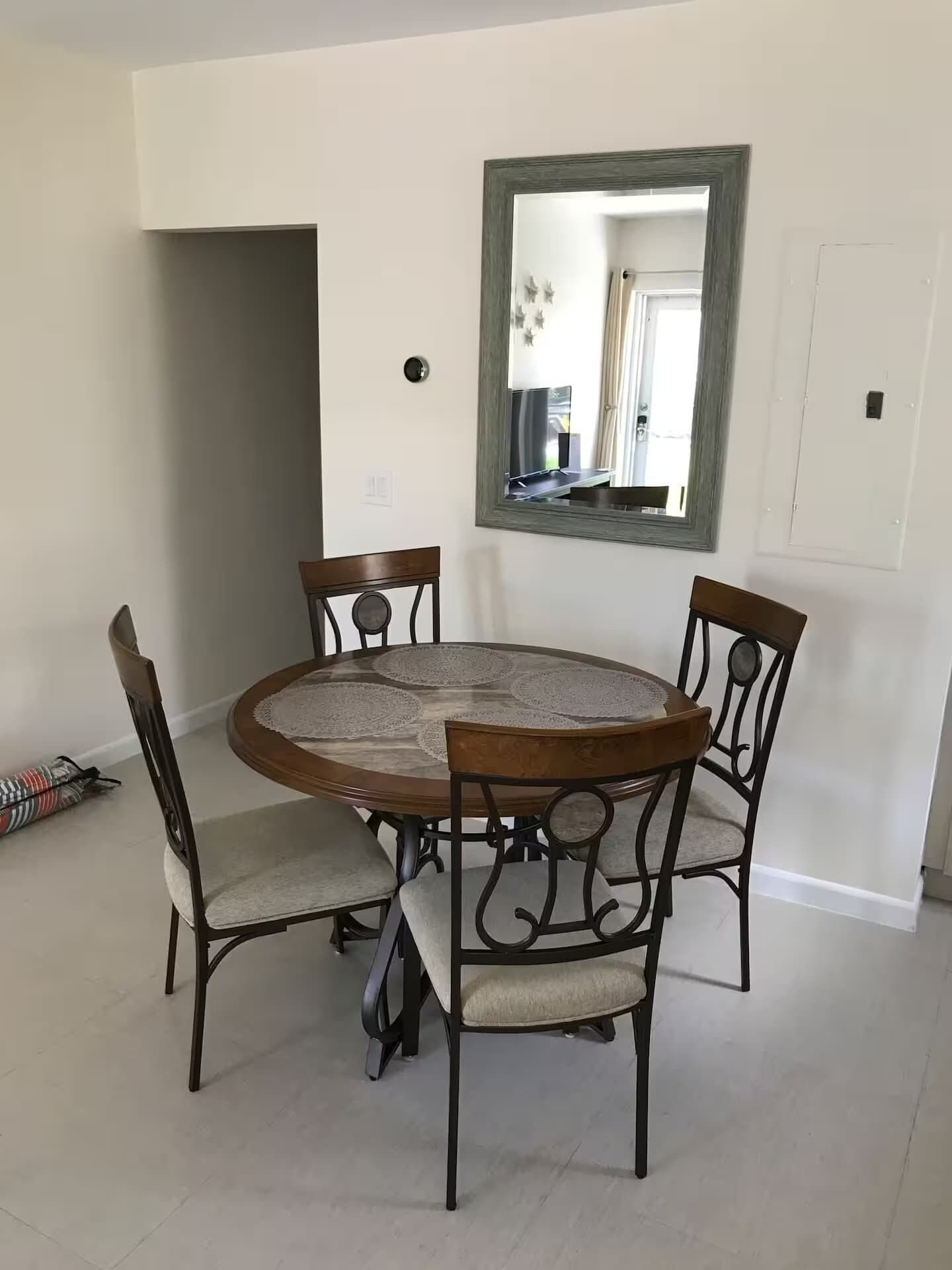 Een eetgedeelte met een ronde tafel, vier stoelen en een spiegel aan de muur.