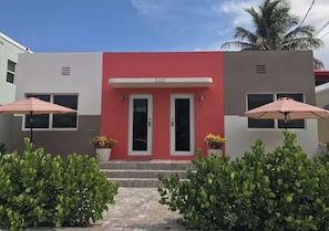 A building with a red facade, two doors, and two windows. There are potted plants and umbrellas in front. - Sun & Sand Retreat 1BR 1BA (Hollywood)