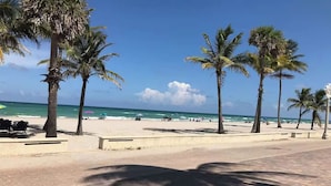 En strand med palmer, en belagt sti og havet i baggrunden.