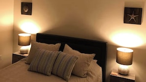 Une chambre à coucher avec un lit, deux lampes de chevet, un ventilateur de plafond et des œuvres d’art murales.