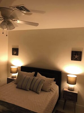 Quarto com cama, duas luminárias de cabeceira, ventoinha no teto e decoração nas paredes.
