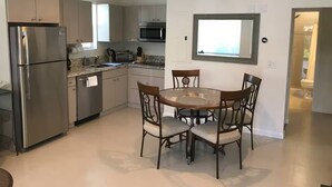 Une cuisine moderne équipée d’appareils électroménagers en acier inoxydable, un coin repas avec une table ronde et des chaises, et une vue sur l’extérieur par une fenêtre.