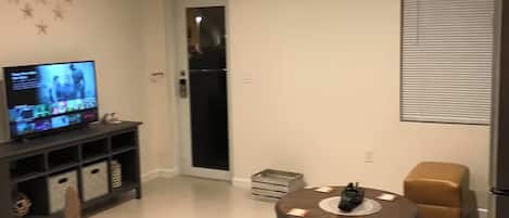 Una sala de estar moderna con una televisión de pantalla plana, una mesa de comedor con sillas, una mesa de centro y un refrigerador.