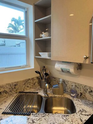 A kitchen with a double stainless steel sink, a window with a view of palm trees, and a marble countertop. - Beachside Comfort 2BR and 2BA  with Outdoor Dining (Hollywood)
