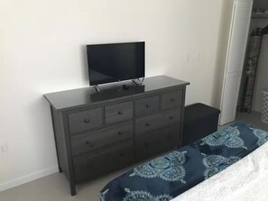 A bedroom with a dark dresser, a flat-screen TV, and a bed with a patterned bedspread. - Beachside Comfort 2BR and 2BA  with Outdoor Dining (Hollywood)