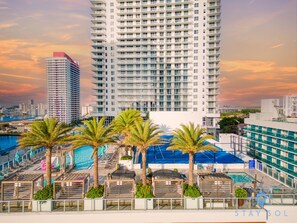 A rooftop pool area with palm trees, lounge chairs, and a view of high-rise buildings. - Modern 2BD 2BA Resort Luxury Bay Corner Views (Hollywood)