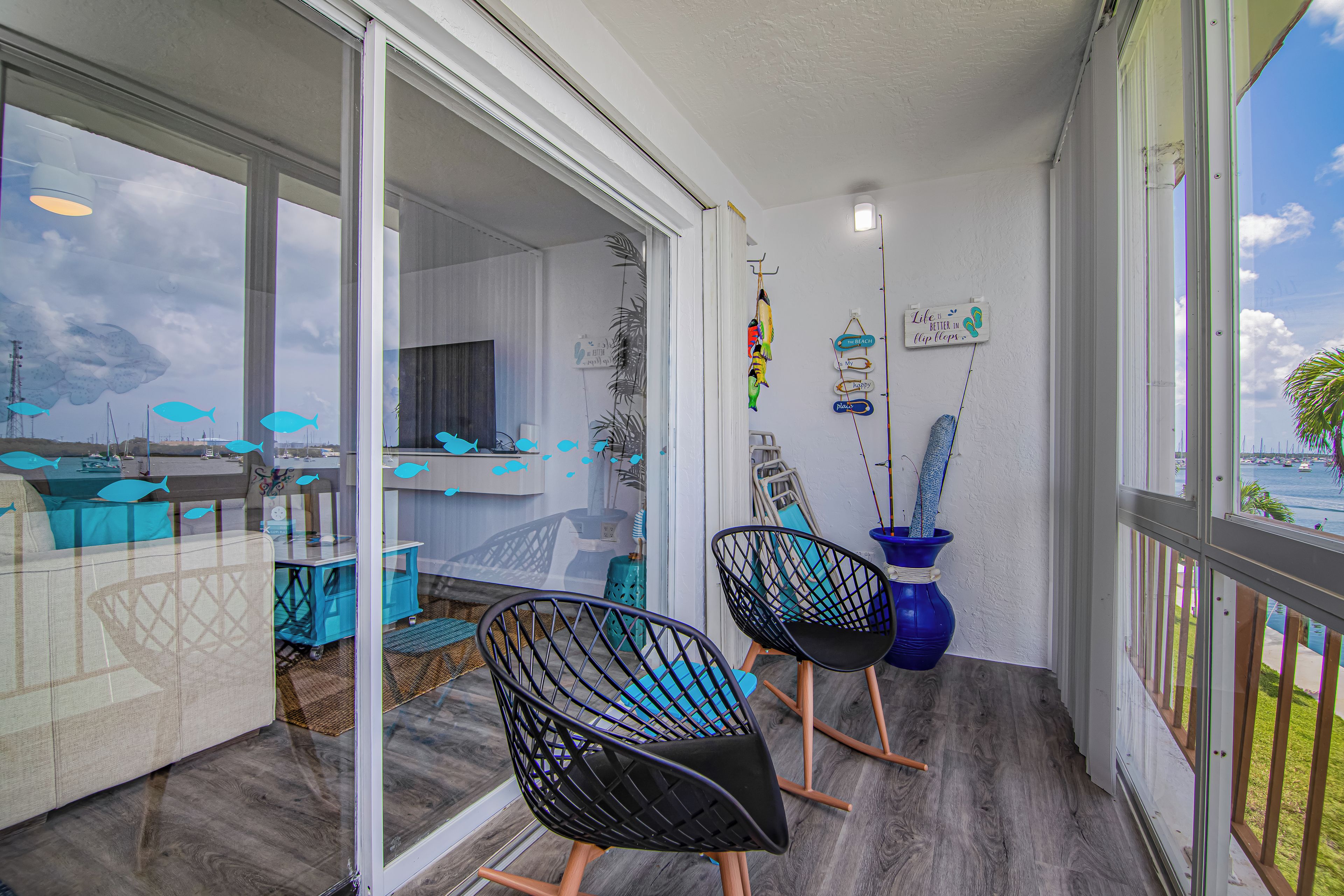 A balcony with a view of the sea, a dining area with a table and chairs, and a wall with decorative items.