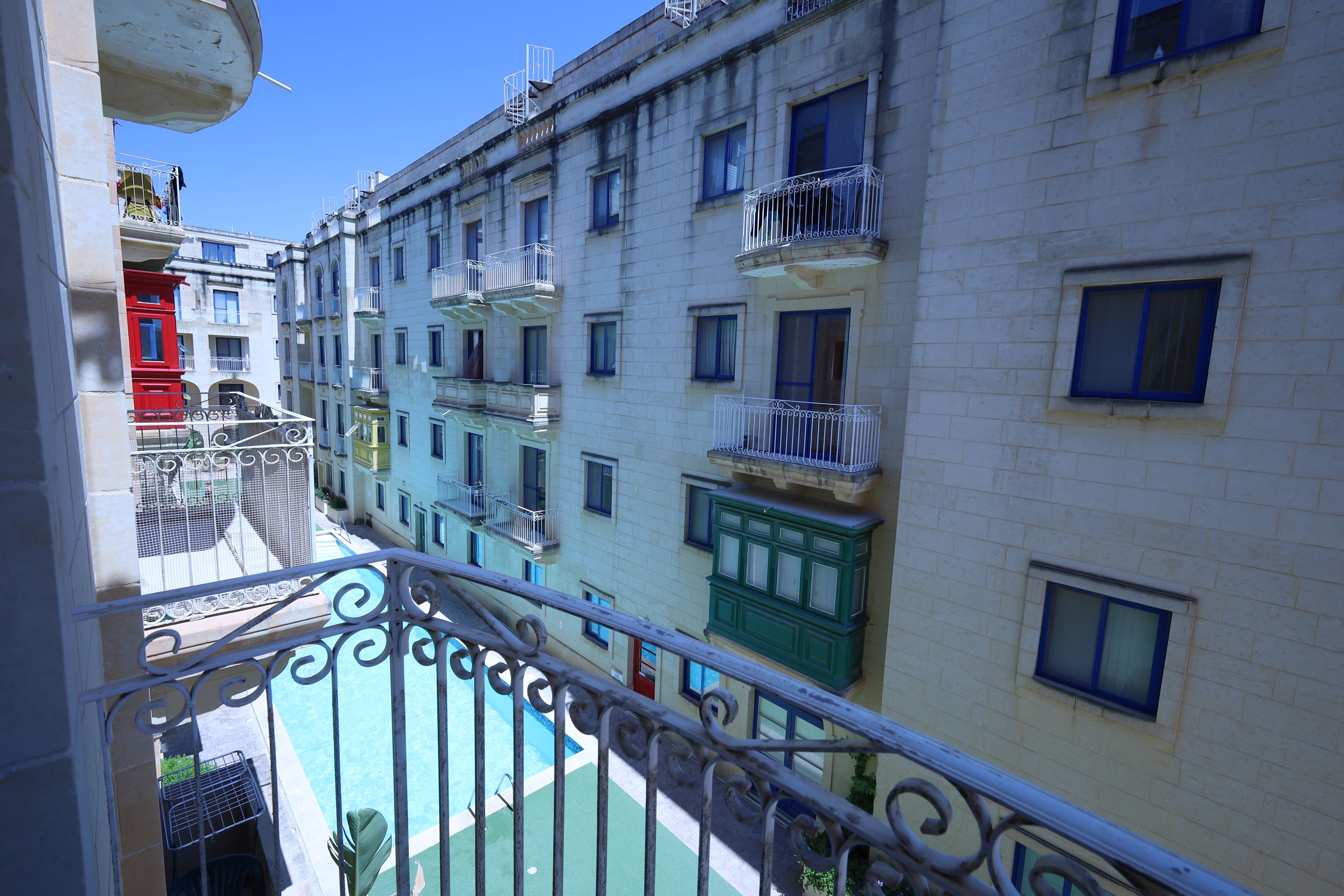 A multi-story building with balconies, a pool, and a clear sky.