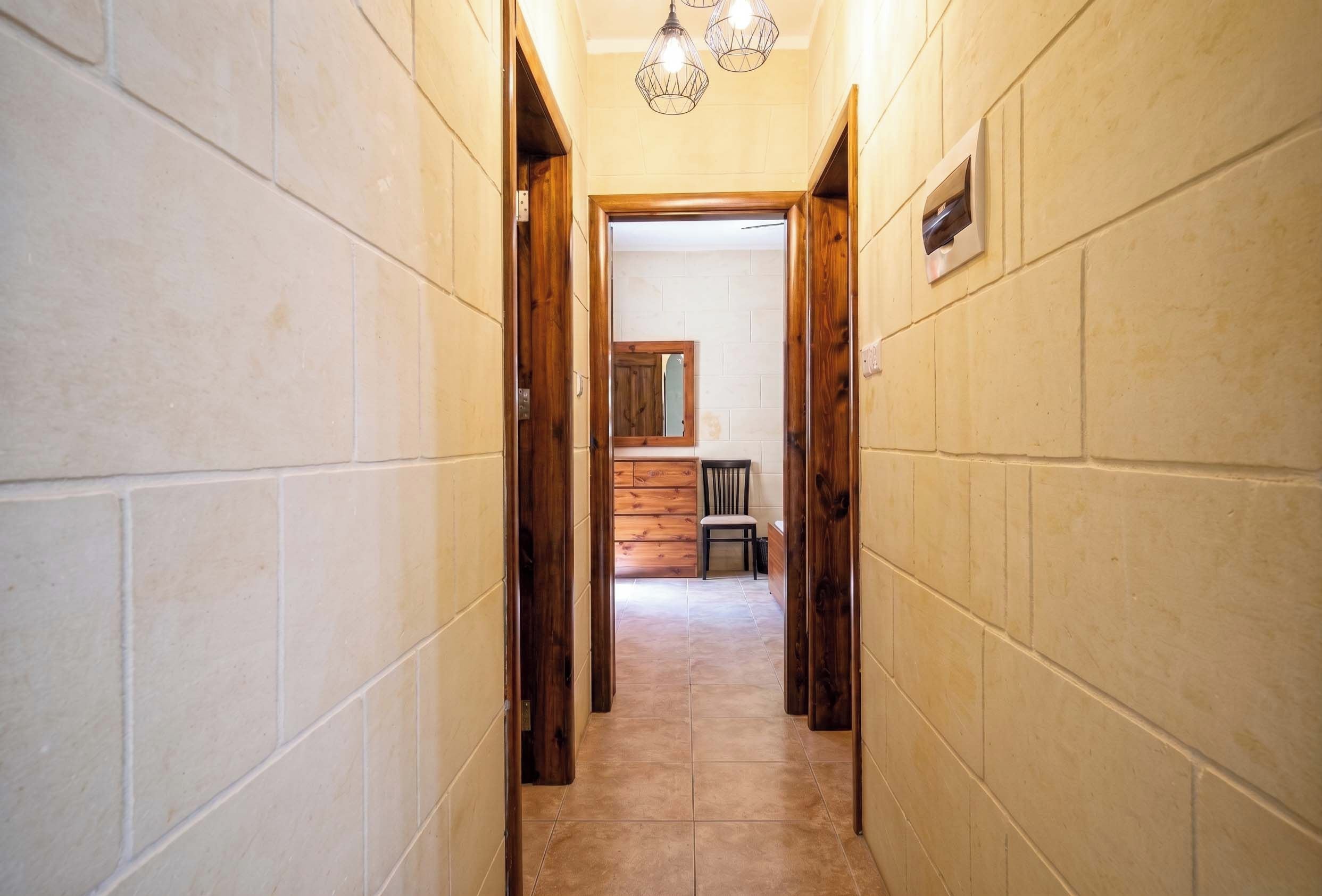 Un couloir aux murs recouverts de carreaux, avec un chambranle de porte en bois et un luminaire.