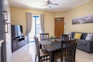 A room with a dining table, chairs, a television, a ceiling fan, and a door marked 'Exit'.