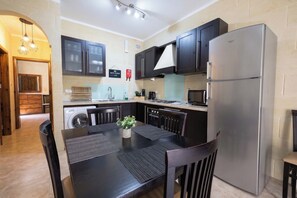 A modern kitchen with dark cabinets, a stainless steel refrigerator, and a dining area with a table and chairs.