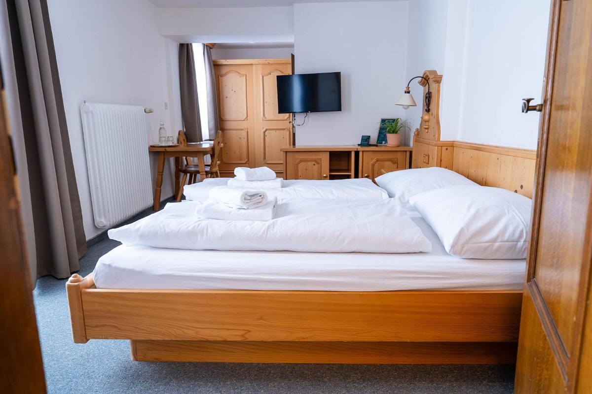 A hotel room with a wooden bed, a flat-screen TV mounted on the wall, a desk with a chair, and a radiator.