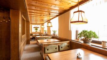 A restaurant interior with wooden tables and benches, hanging pendant lights, and potted plants.