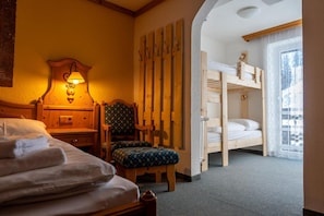 A hotel room with a bed, a chair, a wooden headboard, a wall-mounted lamp, and a bunk bed.